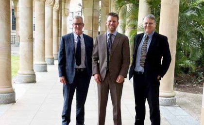 Three men in suits standing in UQ's Great Court. 